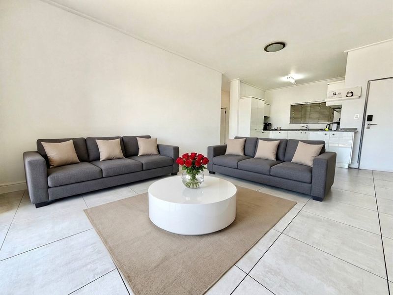 Open-plan living area featuring neutral tiled flooring and a functional kitchen with white cabinetry, creating a bright and cohesive living space.