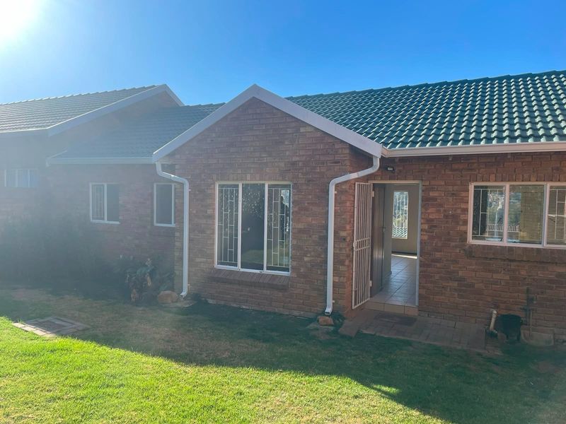 Rear view of a face brick townhouse featuring a tiled roof, security gates, and a small garden area.
