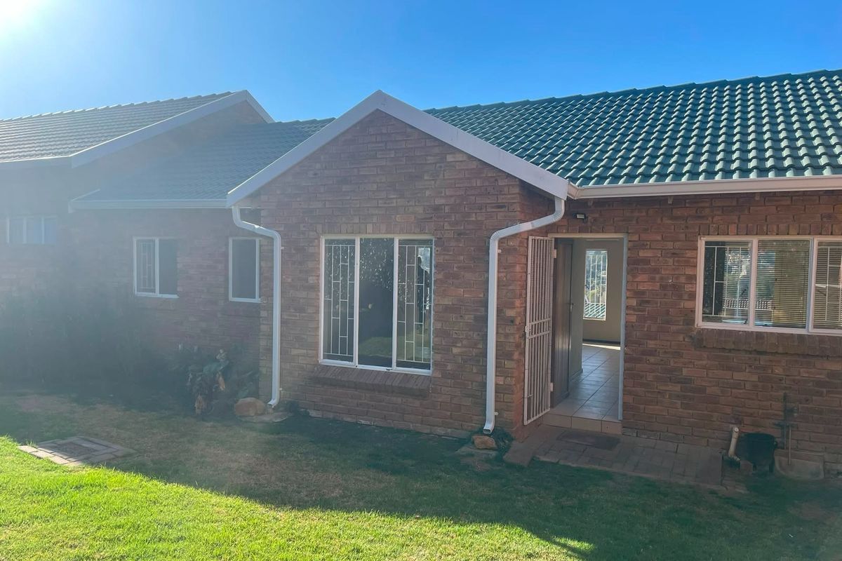 Rear view of a face brick townhouse featuring a tiled roof, security gates, and a small garden area.