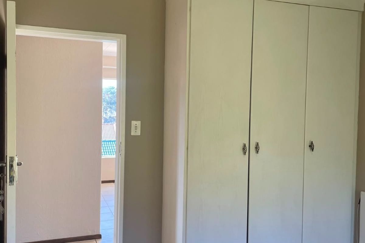 A bedroom featuring built-in wardrobes, carpet flooring, and a coved ceiling, with a doorway leading to an adjacent tiled hallway.