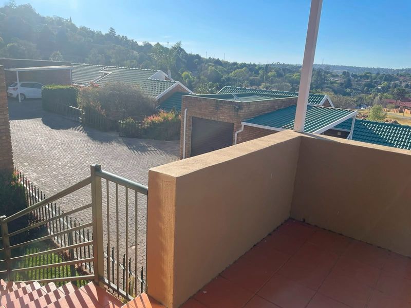 An elevated balcony area featuring tiled flooring and metal balustrades, offering an open view over the townhouse complex and surrounding landscape.