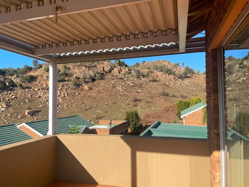A covered balcony featuring tiled flooring and brick accents, offering scenic views of the surrounding rocky landscape and neighborhood.