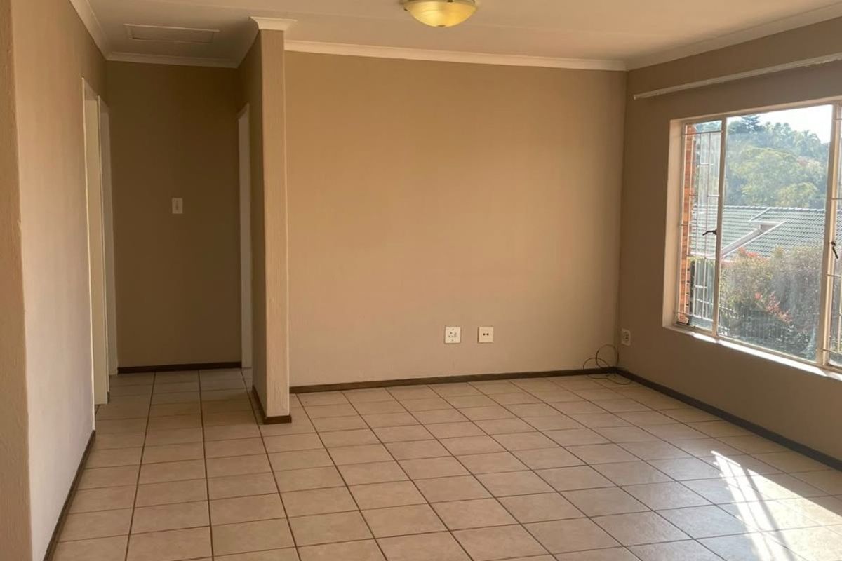 A bright, empty living room featuring neutral wall tones, ceramic floor tiles, and large windows with security bars, offering a clean canvas for personalization.