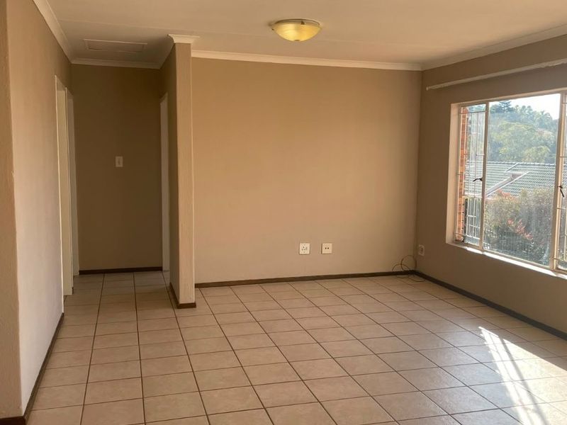 A bright, empty living room featuring neutral wall tones, ceramic floor tiles, and large windows with security bars, offering a clean canvas for personalization.