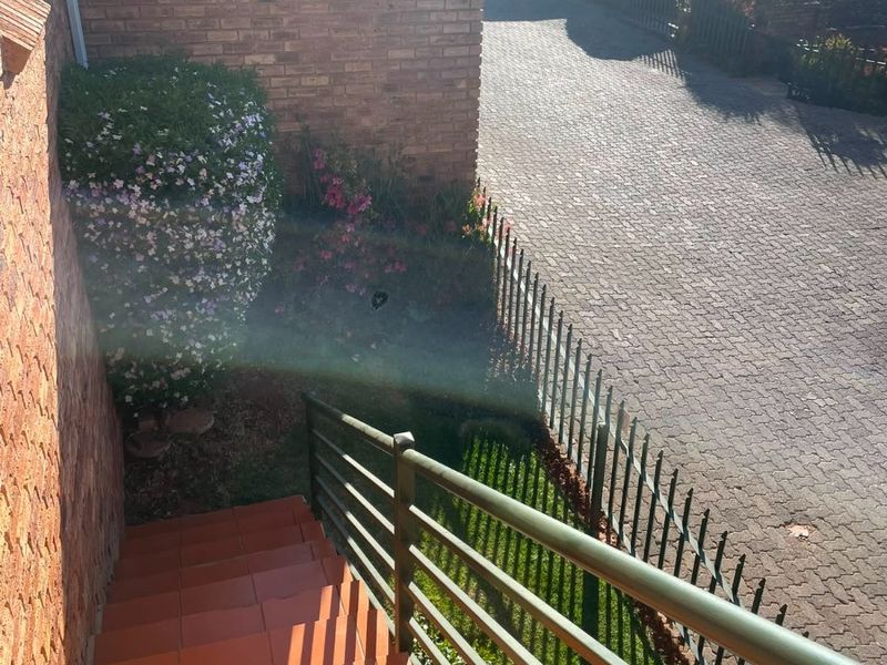 An elevated view of the townhouse entrance featuring a tiled staircase with metal railings, overlooking a paved driveway and landscaped garden area.