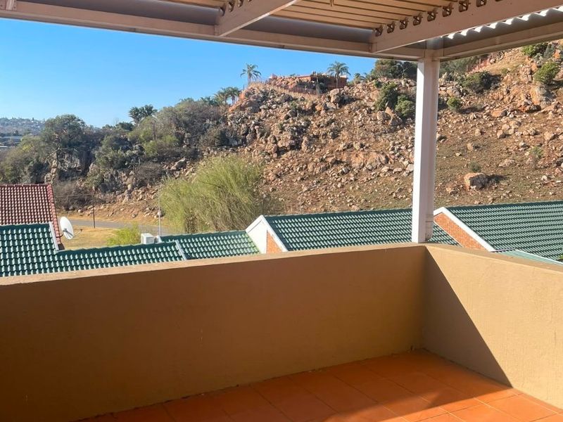 A covered balcony featuring tiled flooring and a solid balustrade, offering elevated views of the surrounding landscape and rocky hillside.