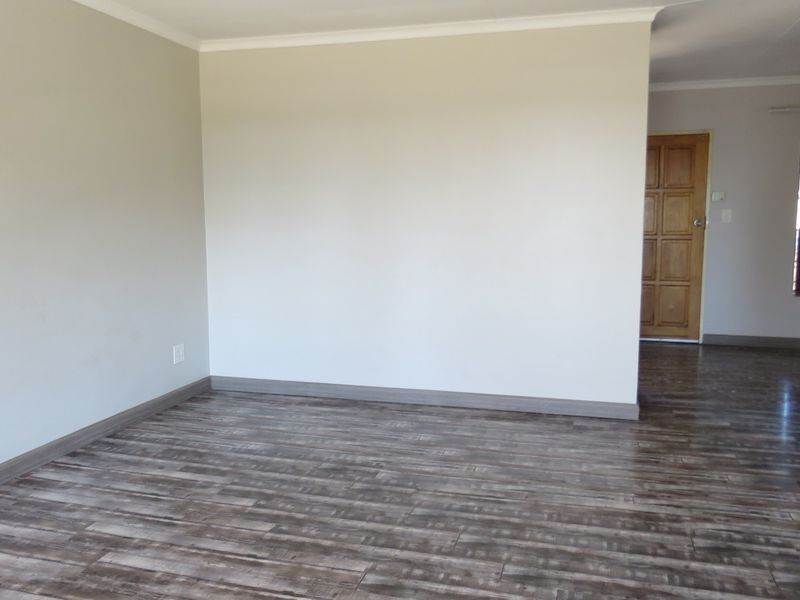 A bright, empty living area featuring modern laminate wood-look flooring, neutral wall tones, and a classic timber door leading to an adjacent space.