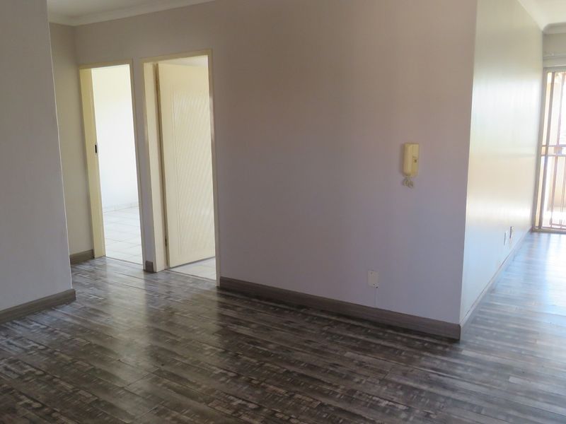 An empty living area featuring modern laminate flooring, an intercom system, and a sliding glass door leading to an outdoor space.