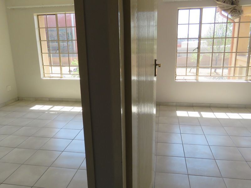 A vacant bedroom featuring tiled flooring and large windows with security bars, offering a blank canvas for interior design.