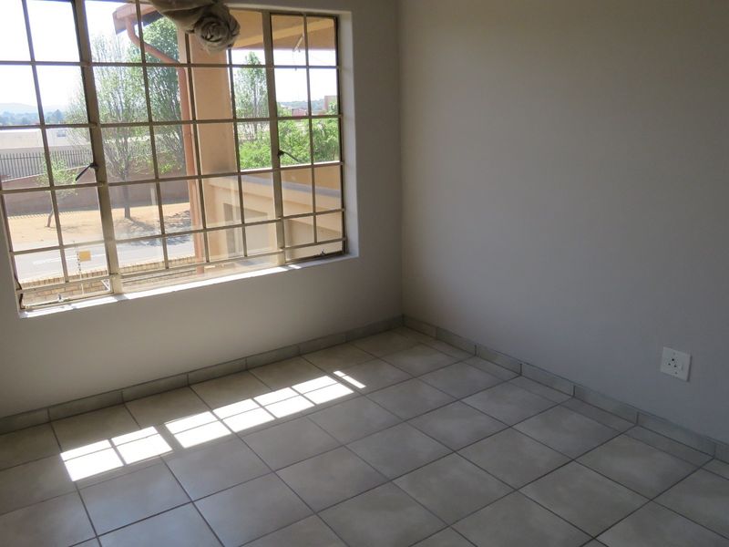 A bright, empty bedroom featuring neutral tiled flooring and large windows fitted with security bars, offering a clean canvas for personalization.
