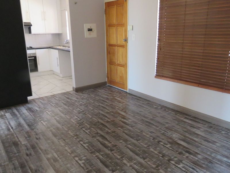 An open-plan living area featuring modern laminate flooring, adjacent to a functional kitchen with built-in cabinetry, oven, and extractor fan.