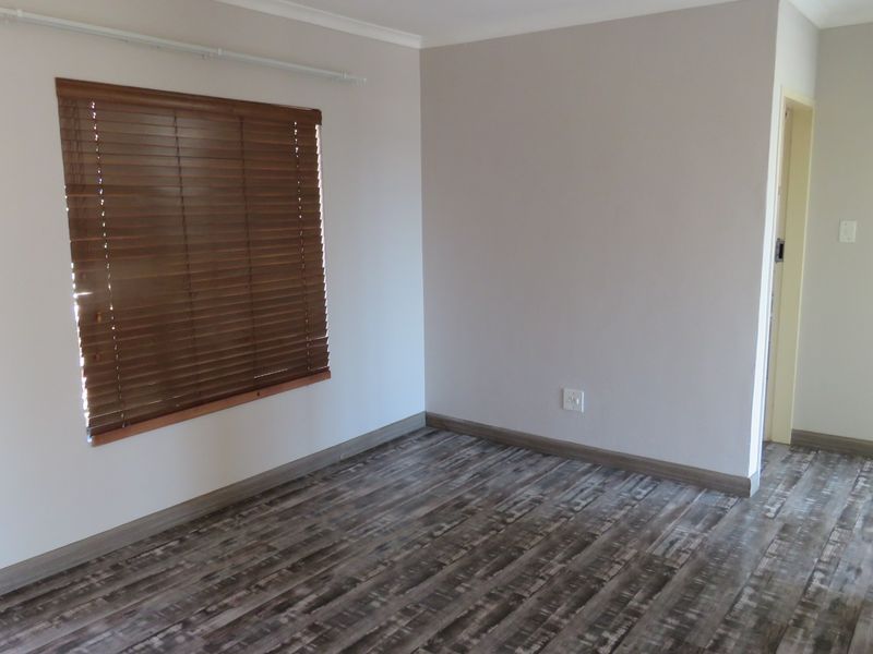 A bright, empty bedroom featuring modern laminate flooring, neutral wall tones, and fitted wooden venetian blinds.