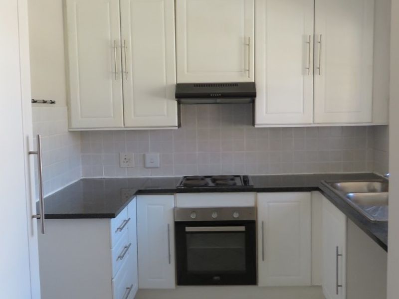 A compact, functional kitchen featuring white cabinetry, dark granite countertops, built-in oven, hob, extractor fan, and tiled flooring.