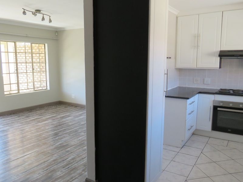 Open plan living area and kitchen featuring modern white cabinetry, built-in oven, hob, extractor fan, and a mix of tiled and laminate flooring.
