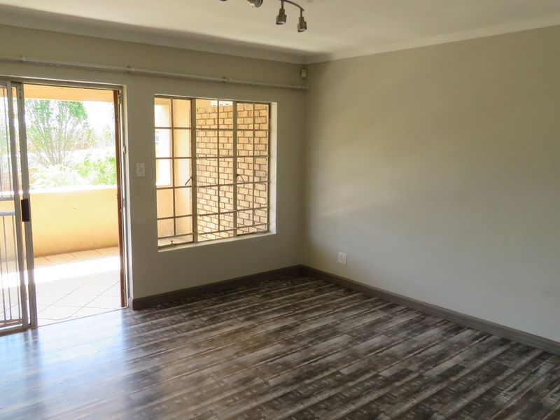 An empty living room featuring laminate flooring, neutral walls, and a sliding door leading to a balcony with security gates.