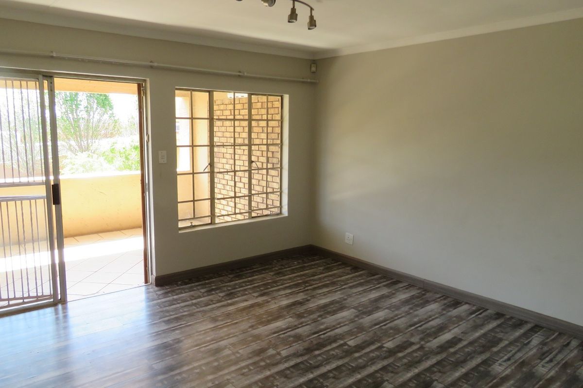 An empty living room featuring laminate flooring, neutral walls, and a sliding door leading to a balcony with security gates.