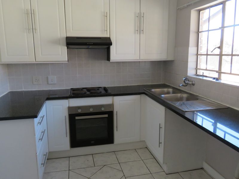 A clean, functional kitchen featuring white cabinetry, black granite countertops, a built-in oven, electric hob, and a double sink with tiled finishes.