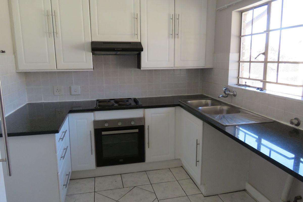 A clean, functional kitchen featuring white cabinetry, black granite countertops, a built-in oven, electric hob, and a double sink with tiled finishes.