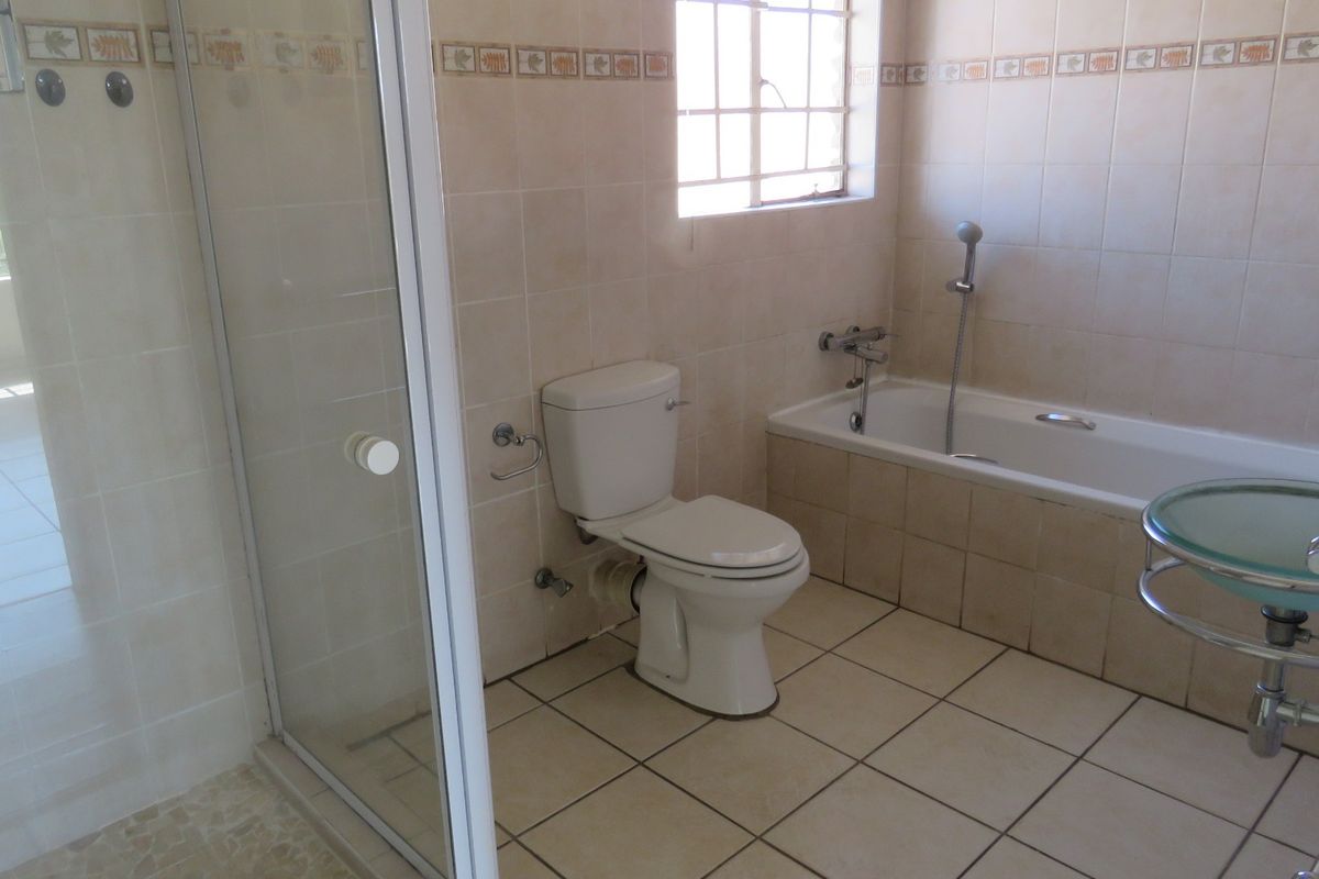 A functional bathroom featuring a shower enclosure, bathtub, toilet, and wall-mounted basin with neutral tiled finishes throughout.