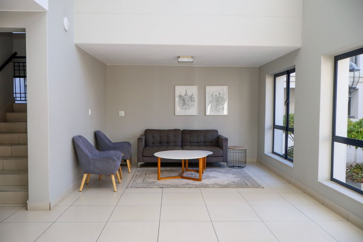 A bright and spacious living area featuring neutral tiled flooring, large windows for natural light, and an adjacent staircase.