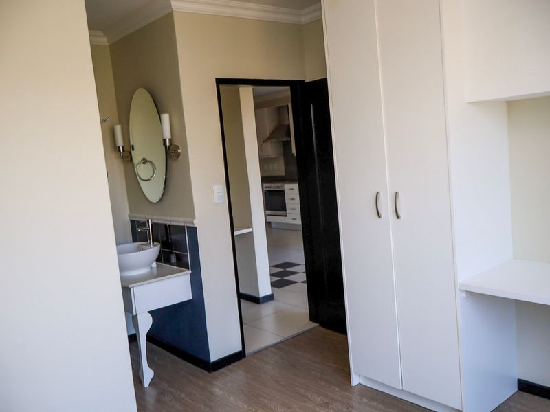 A bedroom featuring a built-in wardrobe, a vanity basin area, and a built-in desk, with a view through to the kitchen.