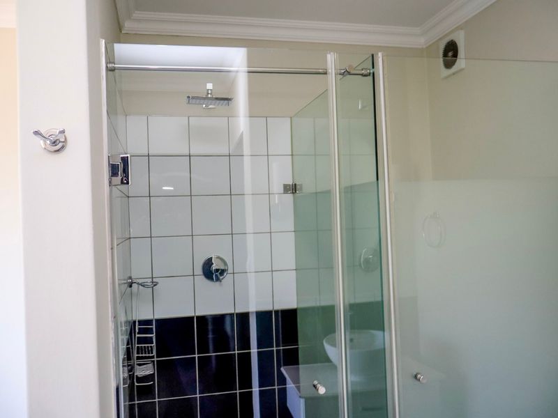 A clean, modern bathroom featuring a glass-enclosed shower with a rain shower head, contrasting black and white wall tiles, and an integrated extractor fan.