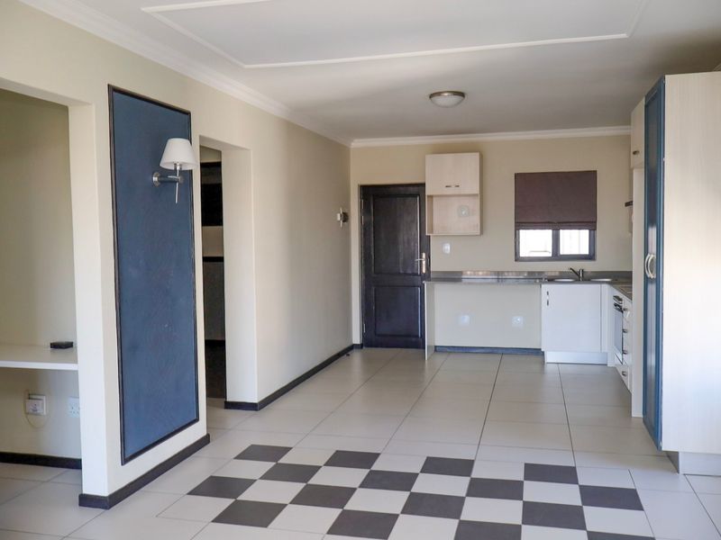 An open-plan living and kitchen area featuring tiled floors, built-in cabinetry, and integrated kitchen appliances in a clean, vacant space.