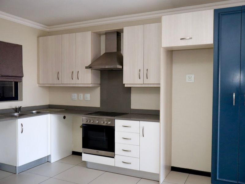 A clean, modern kitchen featuring light wood-tone cabinetry, a built-in oven and hob, stainless steel extractor fan, and neutral tiled flooring.