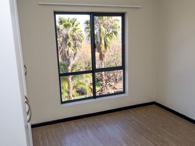 A bright, empty bedroom featuring modern laminate flooring, a built-in wardrobe, and a large window with views of palm trees.