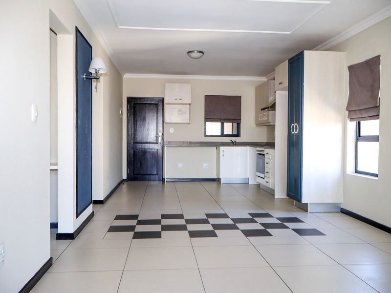 An open-plan living and kitchen area featuring tiled floors, built-in cabinetry, and integrated kitchen appliances in a neutral, well-lit space.