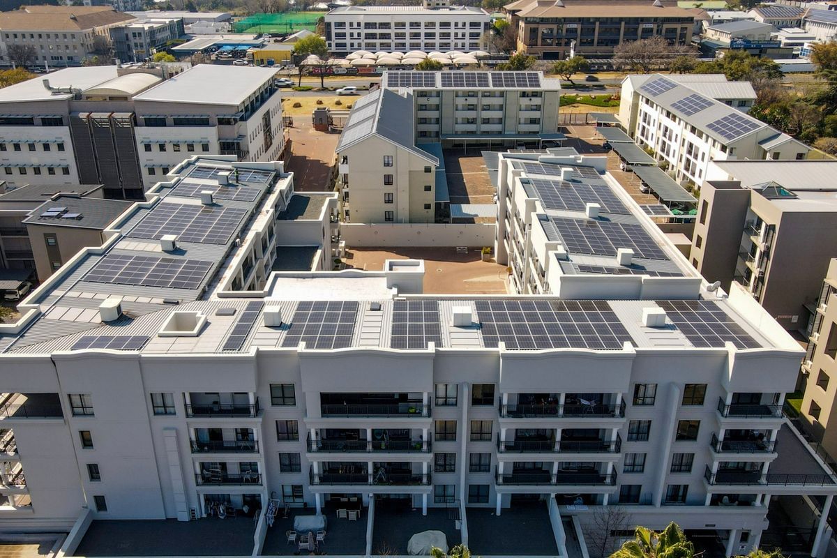 Aerial view of a modern apartment complex featuring extensive rooftop solar panel installations and a central paved courtyard area.