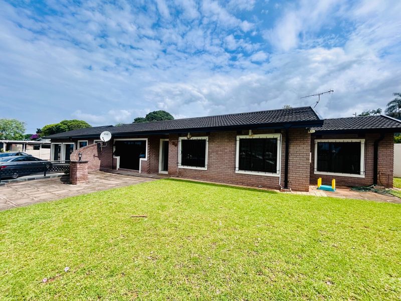A single-story brick house featuring a tiled roof, security bars on windows, and a paved driveway area set against a well-maintained lawn.