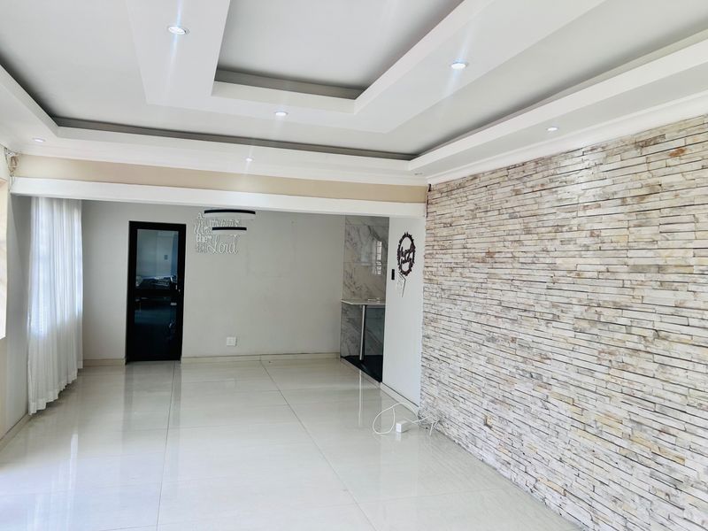 Spacious open-plan living area featuring a modern recessed ceiling with downlights, polished tiled flooring, and a prominent stone-clad feature wall.