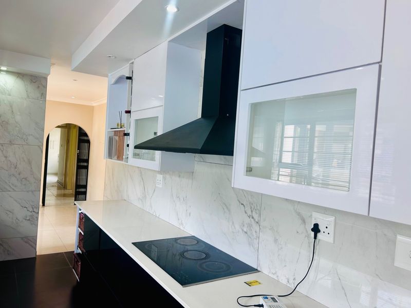 Modern kitchen featuring sleek white cabinetry, marble-look backsplash, stone countertops, and a built-in electric hob with a black extractor fan.