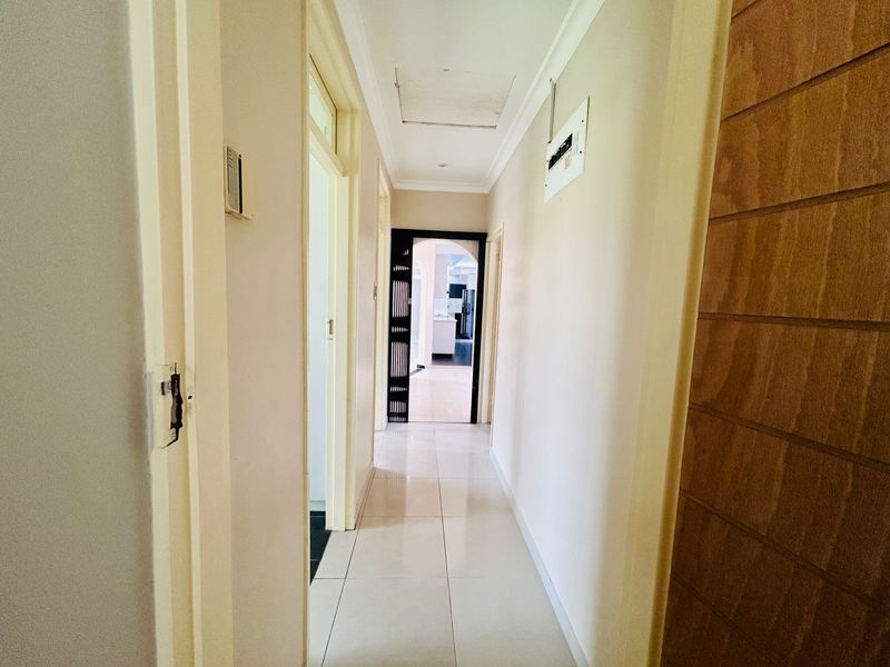 A clean, tiled hallway providing access to multiple rooms, featuring a ceiling access hatch and a wall-mounted electrical distribution board.