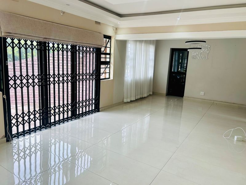 Spacious, light-filled living area featuring polished porcelain floor tiles, recessed ceiling with downlights, and secure sliding door access to the exterior.