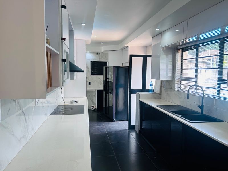 Modern galley-style kitchen featuring high-gloss cabinetry, marble-look countertops, integrated hob, extractor fan, and a sleek double sink with contemporary fixtures.