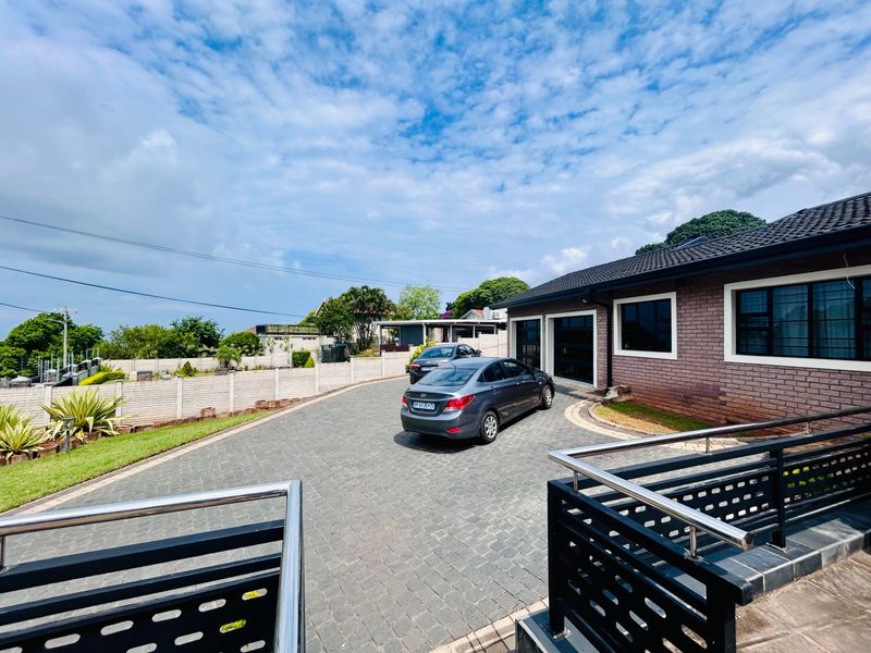 Front exterior view of the property featuring a paved driveway, brick facade, and secure boundary wall with modern metal railings.