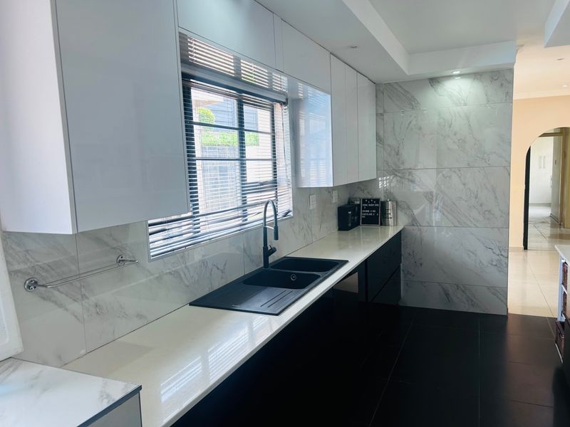 Modern kitchen featuring sleek white cabinetry, marble-look wall tiling, quartz countertops, and a contemporary black double basin sink with matching tapware.
