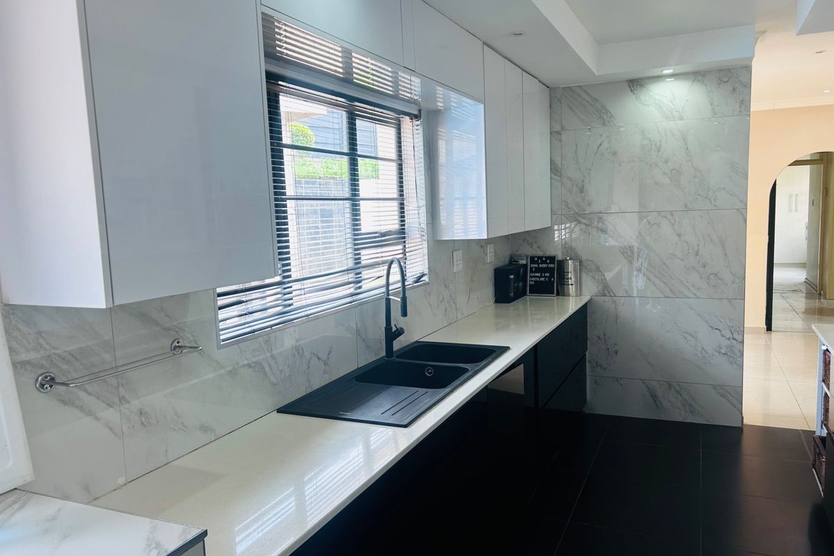 Modern kitchen featuring sleek white cabinetry, marble-look wall tiling, quartz countertops, and a contemporary black double basin sink with matching tapware.