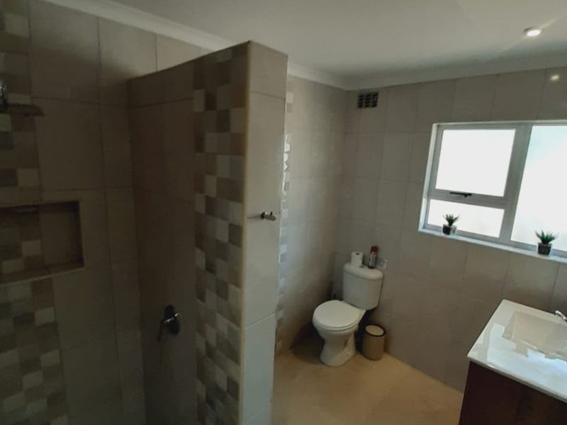 A functional bathroom featuring a walk-in shower with a built-in niche, a vanity unit, and a toilet, finished with neutral wall tiles.