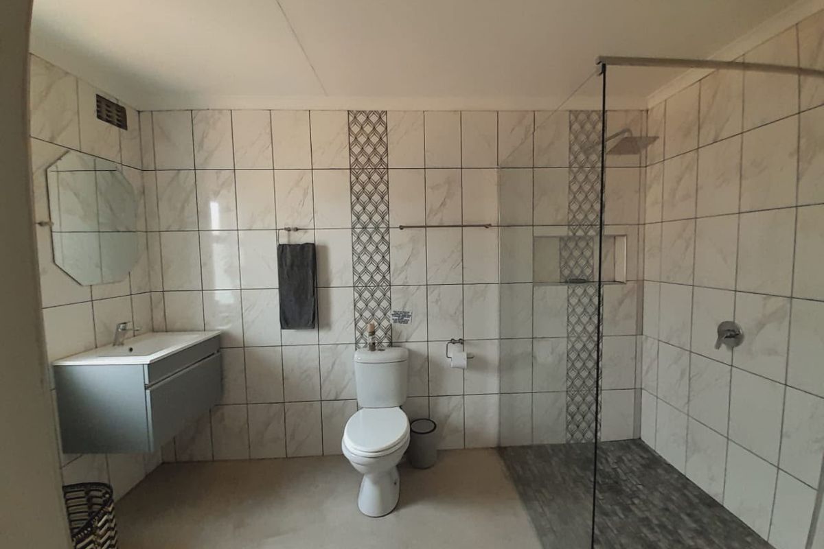 Modern bathroom featuring a wall-mounted vanity, a spacious walk-in shower with a glass screen, and contemporary marble-look wall tiling.