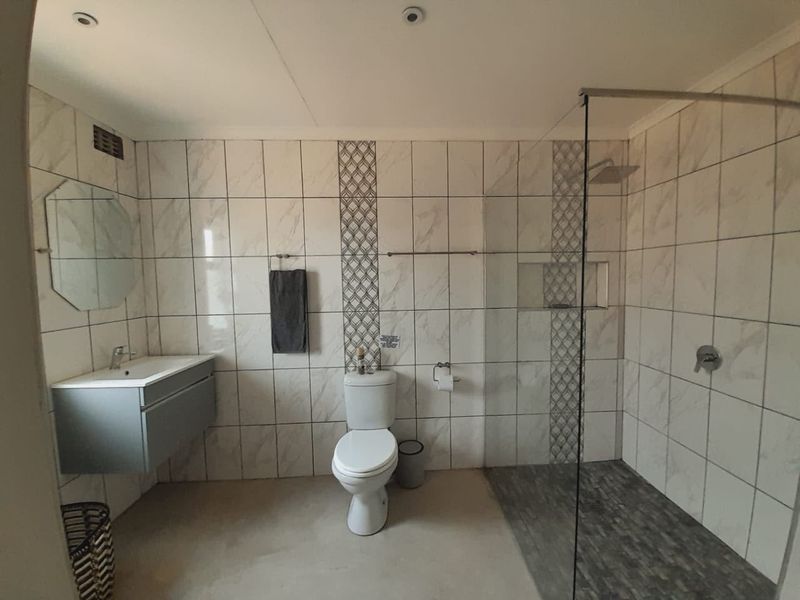 Modern bathroom featuring a wall-mounted vanity, a spacious walk-in shower with a glass screen, and contemporary marble-look wall tiling.