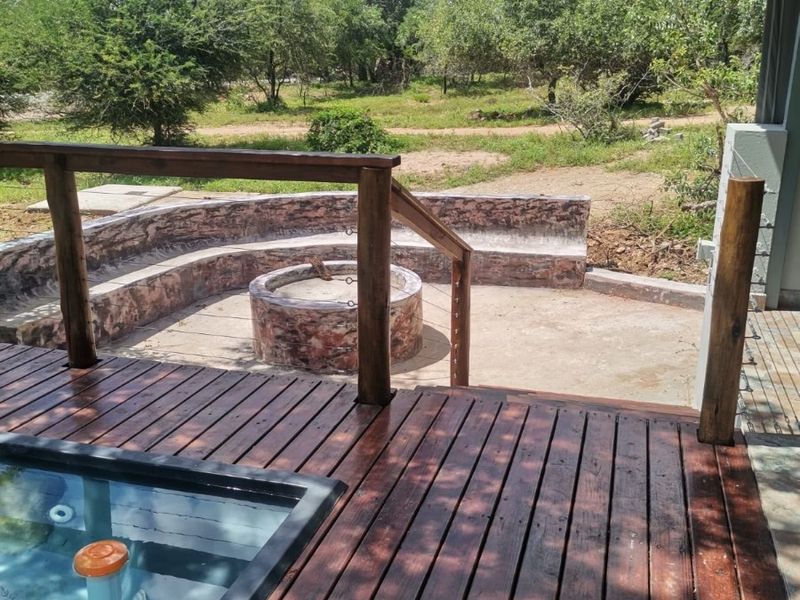 Outdoor entertainment area featuring a timber deck, built-in plunge pool, and a curved stone fire pit seating area overlooking the natural bushveld.