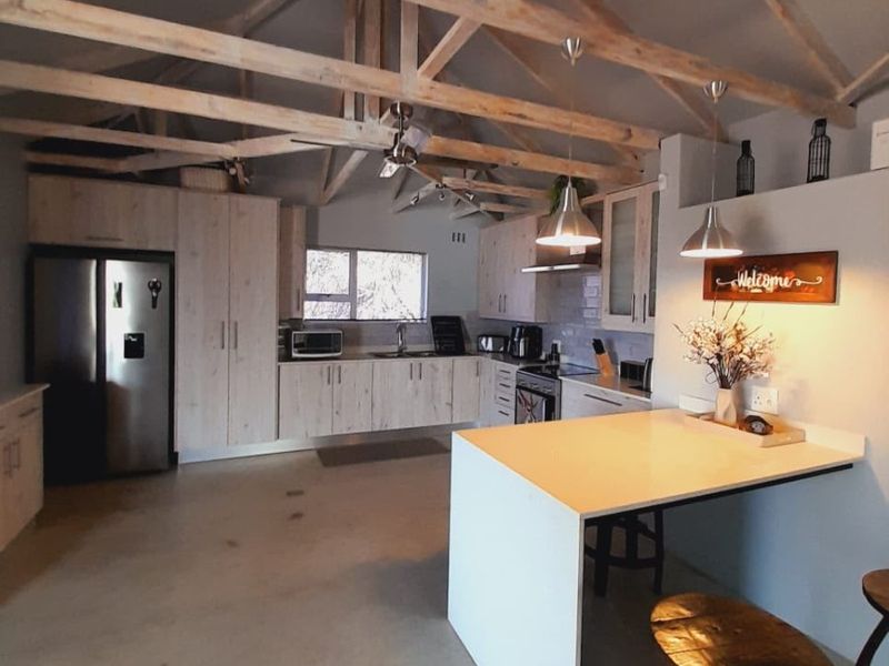 Spacious kitchen featuring exposed timber roof trusses, modern built-in cabinetry, a functional island, and polished concrete flooring in a bright, open-plan layout.