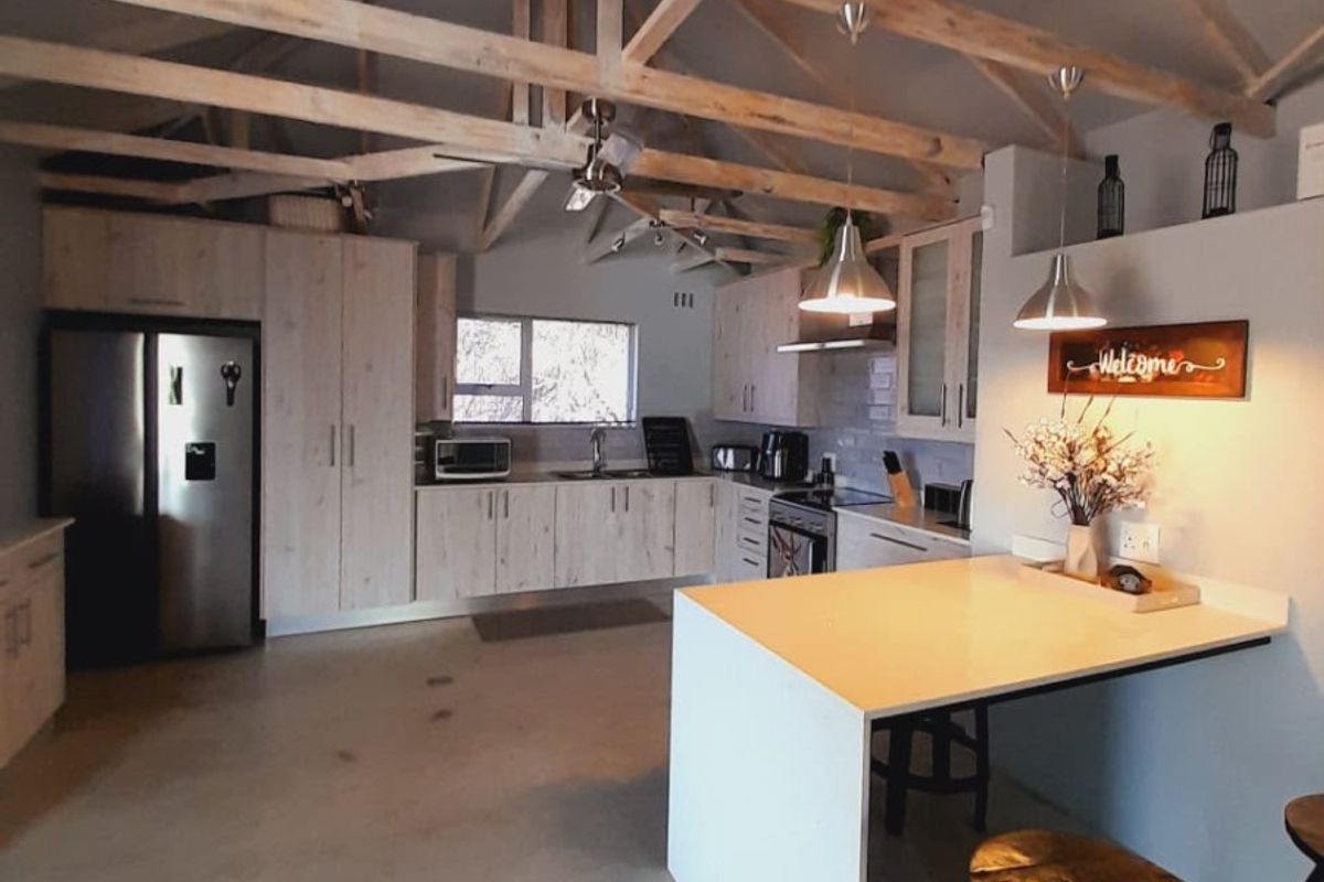 Spacious kitchen featuring exposed timber roof trusses, modern built-in cabinetry, a functional island, and polished concrete flooring in a bright, open-plan layout.