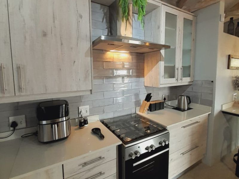 Modern kitchen featuring light wood-grain cabinetry, stone countertops, subway tile backsplash, and exposed timber ceiling beams with a stainless steel gas stove.