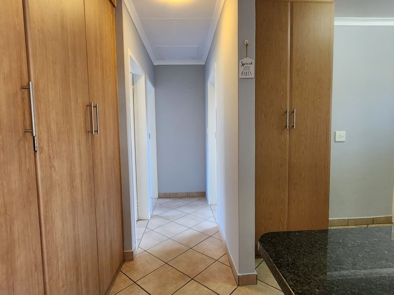 A clean, well-lit hallway featuring neutral tiled flooring and extensive built-in wooden cabinetry for storage, connecting various rooms within the townhouse.