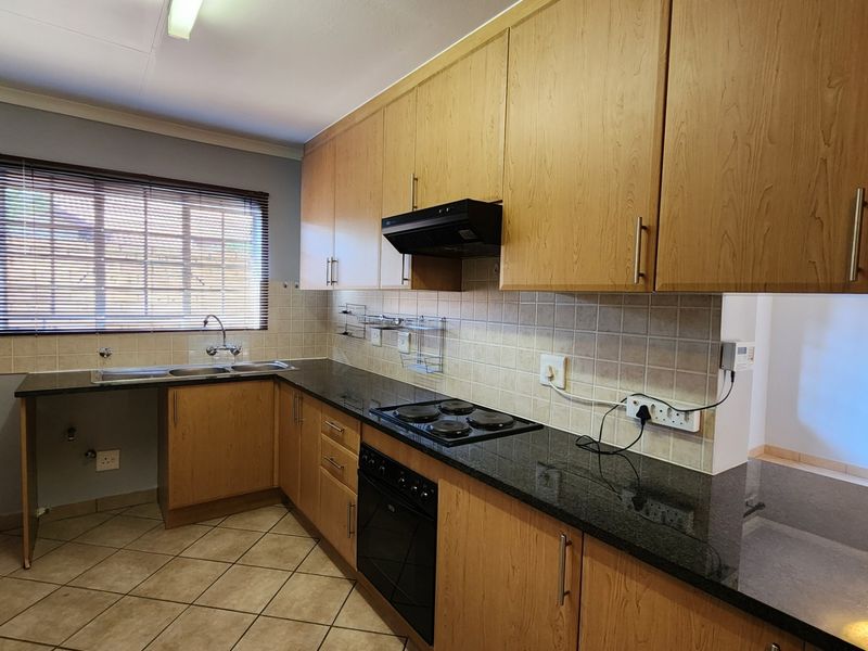 A functional kitchen featuring laminate cabinetry, granite countertops, a built-in oven with hob, and tiled flooring.