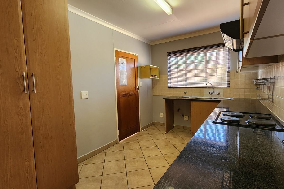 A functional kitchen featuring granite countertops, built-in cabinetry, an electric hob with extractor fan, and tiled flooring.